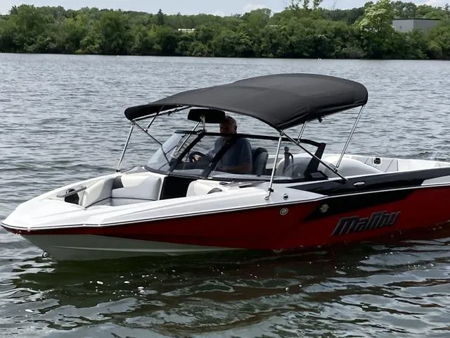 Slide: The Image of 2024 Malibu TXi Mo boat on a lake with a black canopy. - 8