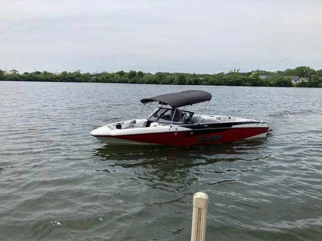 Slide: The Image of 2024 Malibu TXi Mo boat on calm water with lush green shoreline. - 9