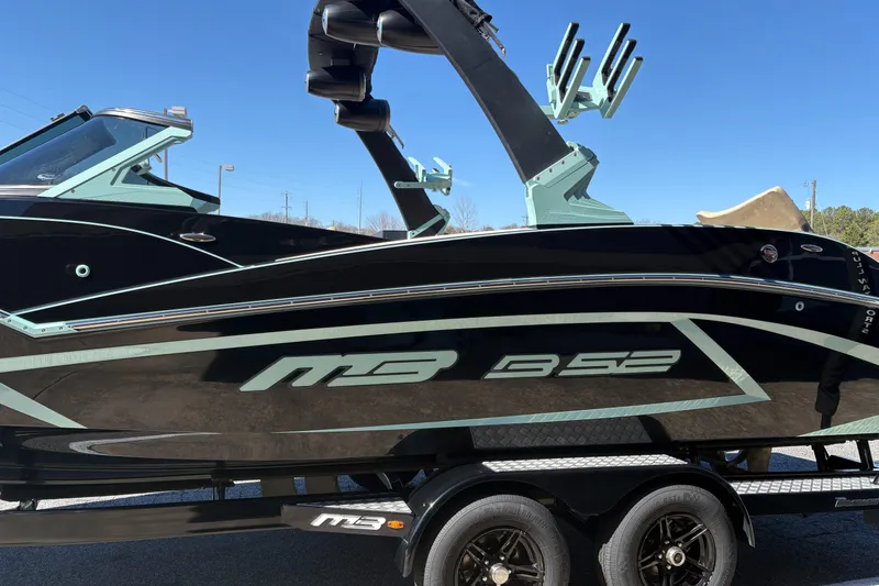 Slide: The Image of 2022 MB B52 Alpha boat on trailer, black with teal accents, under clear blue sky. - 4