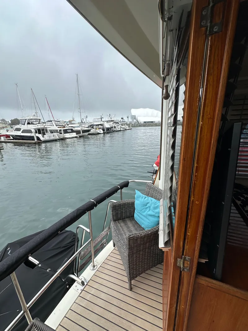 Slide: The Image of 1985 Gulfstar 49 Motor Yacht docked, featuring a cozy deck with wicker chair and blue cushion. - 33