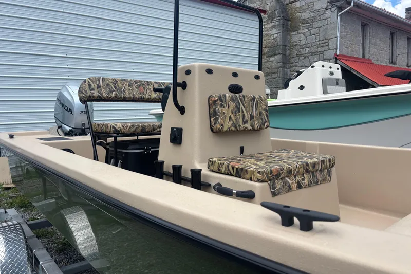 Slide: The Image of 2025 Carolina Skiff E18 JVX CC boat with camouflage seating, parked near a metal building. - 3