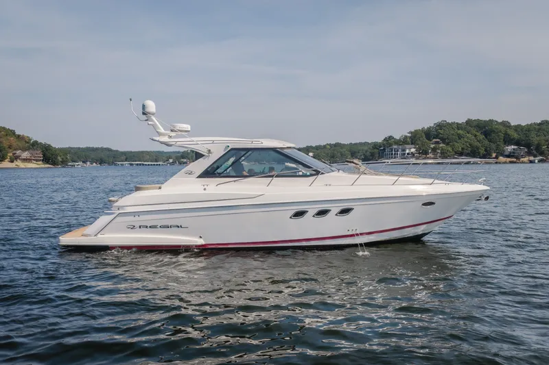 The Image of 2012 Regal 42 Sport Coupe yacht cruising on a serene lake with scenic shoreline. - 1