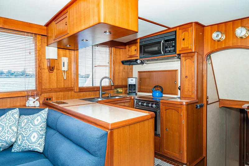 Slide: The Image of 1987 Fleming 50 Raised Pilothouse interior with wooden cabinetry, blue seating, and modern kitchen appliances. - 20
