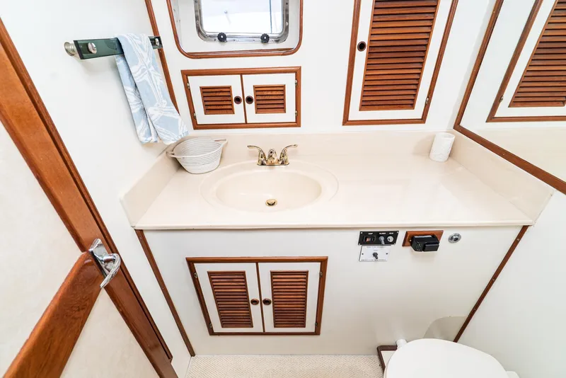 Slide: The Image of 1987 Fleming 50 Raised Pilothouse bathroom with sink, wooden cabinets, and porthole window. - 29