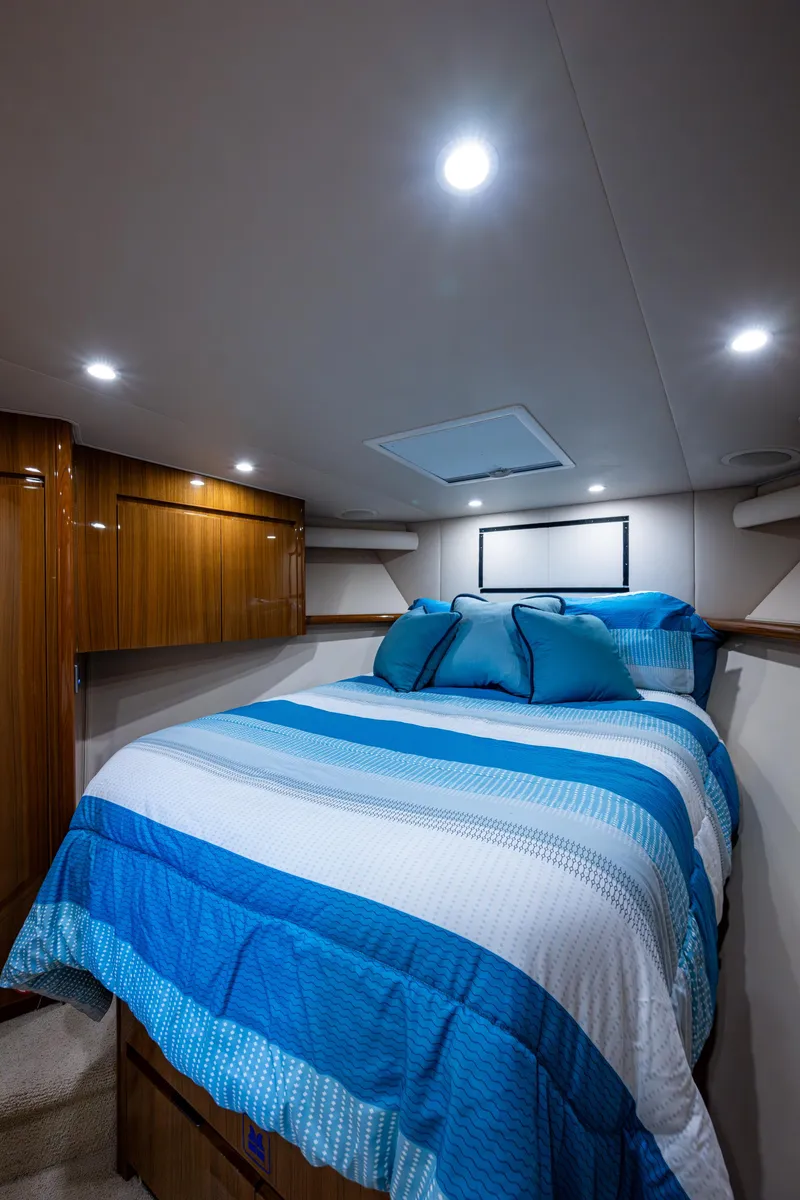 Slide: The Image of 2016 Viking 46 Convertible yacht bedroom with blue bedding and wooden cabinets. - 24