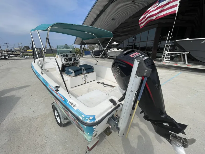 Slide: The Image of 1999 Bayliner 17cc boat with outboard motor and canopy, parked near a building with a flag. - 5