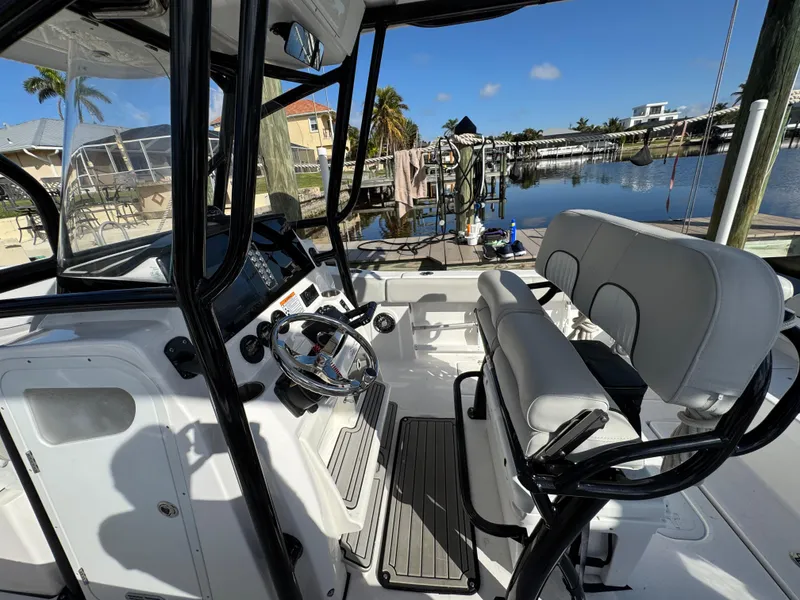 Slide: The Image of 2023 Sea Fox 268 Commander boat interior with steering wheel and seating, docked by a waterfront. - 17