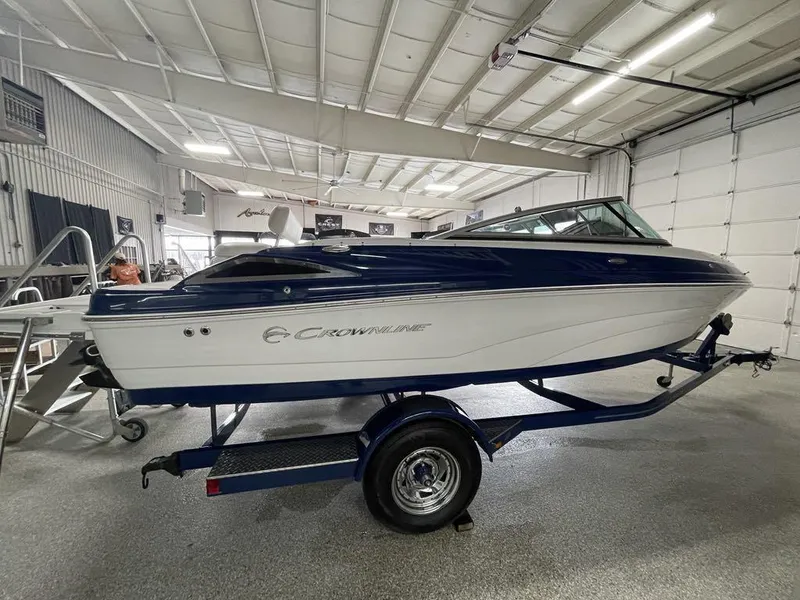 Slide: The Image of 2020 Crownline 205 SS boat in a showroom, blue and white exterior, on a trailer. - 4