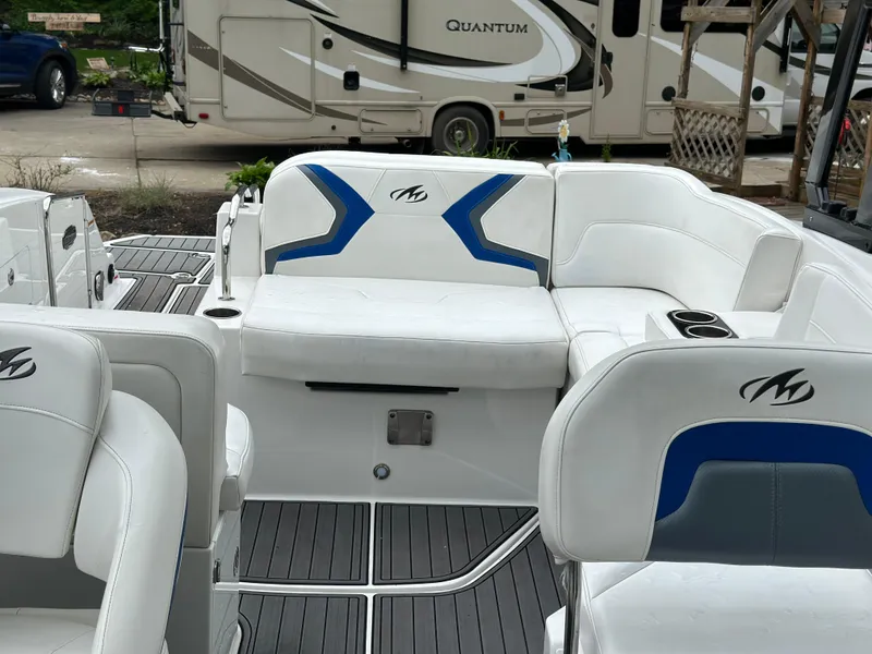 Slide: The Image of 2017 Monterey M6 boat interior with white seating and blue accents, parked near an RV. - 23