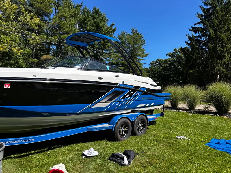Slide: The Image of 2017 Monterey M6 boat on trailer, parked on grass, surrounded by trees and clothing items. - 6