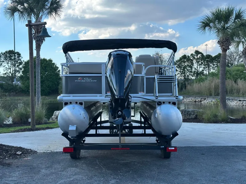 Slide: The Image of 2025 Sun Tracker Party Barge 18 DLX pontoon boat on trailer, parked near palm trees. - 3