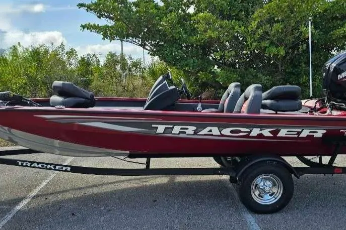 The Image of 2025 Tracker Pro Team 175 boat, red color, parked on a trailer near trees. - 0