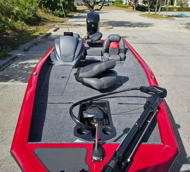 Slide: The Image of 2025 Tracker Pro Team 175 boat with red exterior and gray seating, parked on pavement. - 3