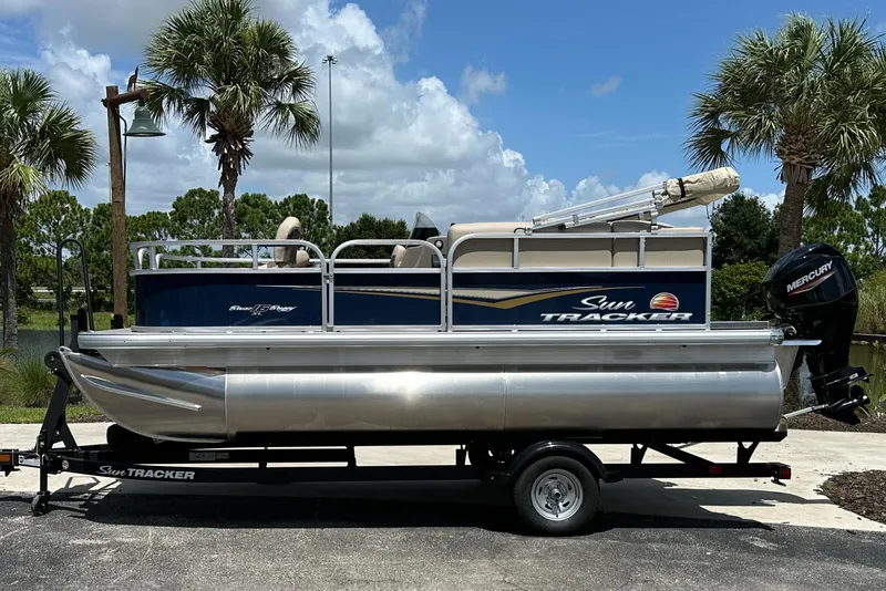 The Image of 2025 Sun Tracker Bass Buggy 16 XL Select pontoon boat on trailer, parked outdoors. - 0