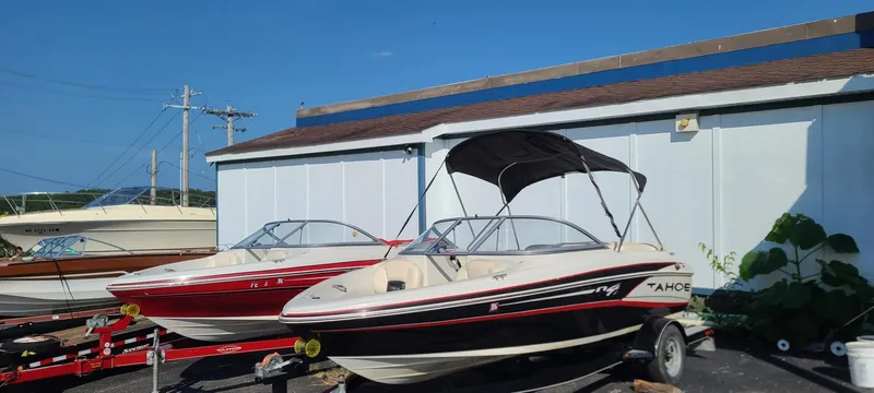 Slide: The Image of 2013 Tahoe Q4i boat with canopy on trailer, parked beside a building. - 2