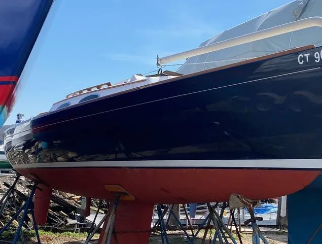 Slide: The Image of 2003 Alerion Express 28 sailboat on stands, blue hull, red bottom, outdoor setting. - 12