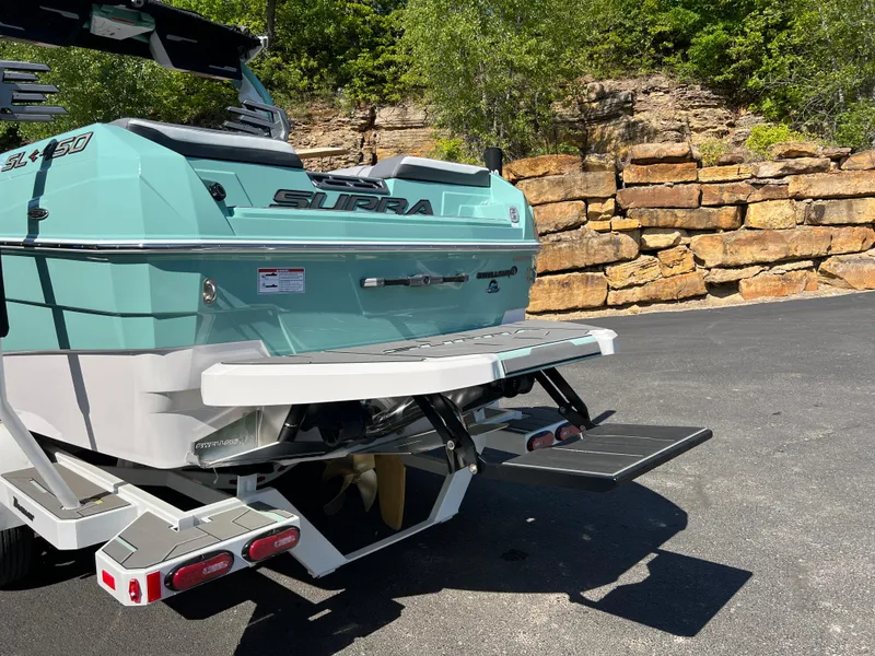 Slide: The Image of 2024 Supra SL boat with teal exterior, parked on pavement near stone wall. - 4