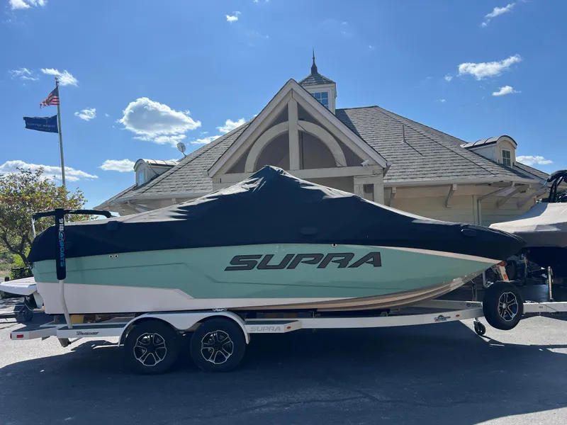 Slide: The Image of 2024 Supra SL boat on trailer, covered, parked near a building under a clear sky. - 5