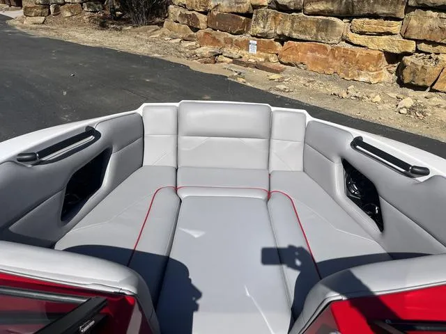 Slide: The Image of 2024 Moomba Mojo boat interior with gray seating and red accents, parked near stone wall. - 13