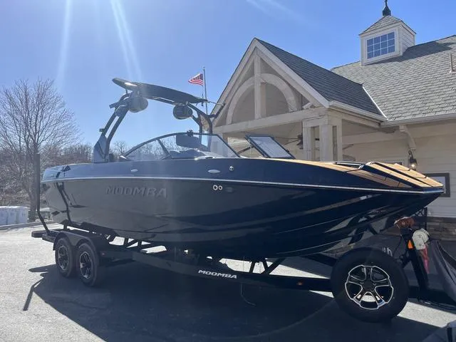 Slide: The Image of 2024 Moomba Mojo boat on trailer, parked near a building under clear blue sky. - 4