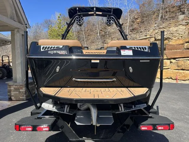 Slide: The Image of 2024 Moomba Mojo boat rear view with black exterior and tan interior, parked outdoors. - 5
