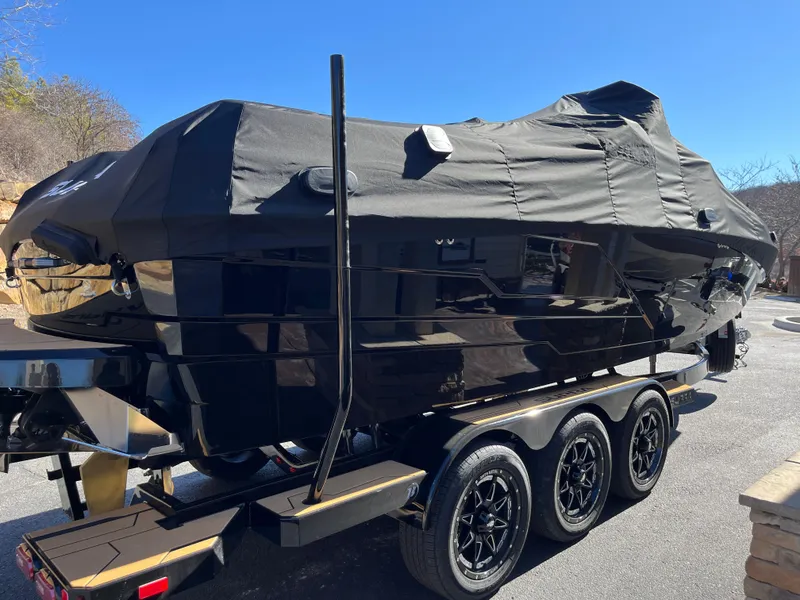 Slide: The Image of 2025 Supra SE boat covered on a triple-axle trailer, parked outdoors. - 31