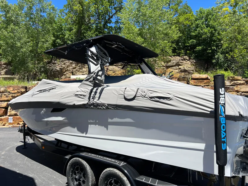 Slide: The Image of 2024 Centurion Fi23 boat with cover on trailer, surrounded by trees and rocks. - 20
