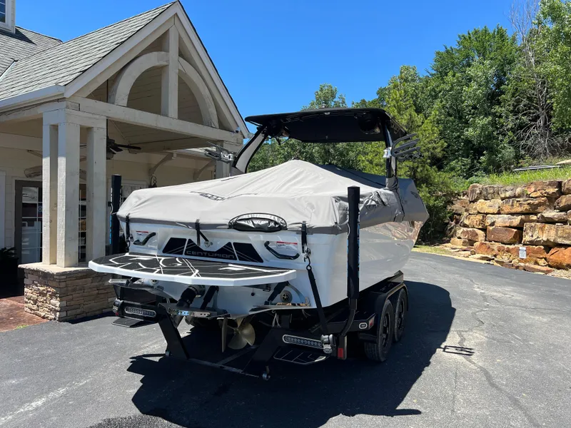 Slide: The Image of 2024 Centurion Fi23 boat covered and parked near a house, sunny day. - 22