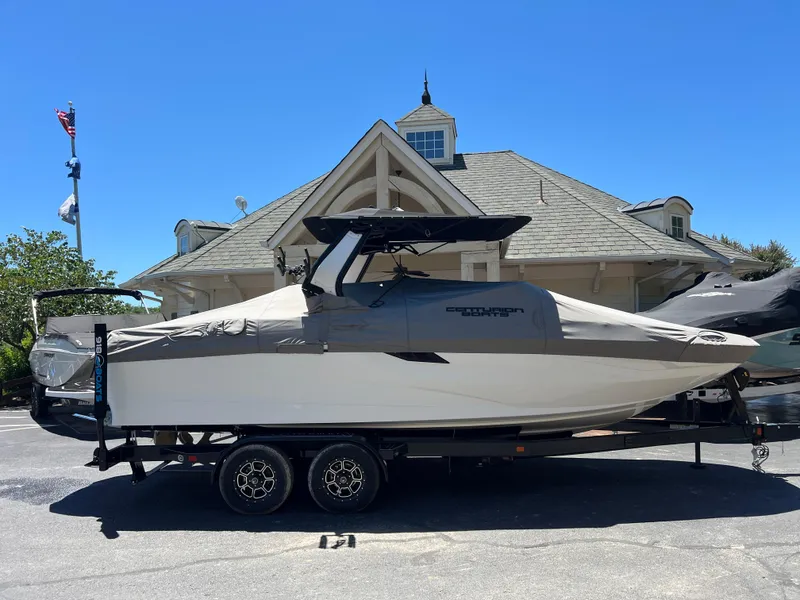 Slide: The Image of 2024 Centurion Fi23 boat on trailer, covered, parked near a building under clear blue sky. - 23