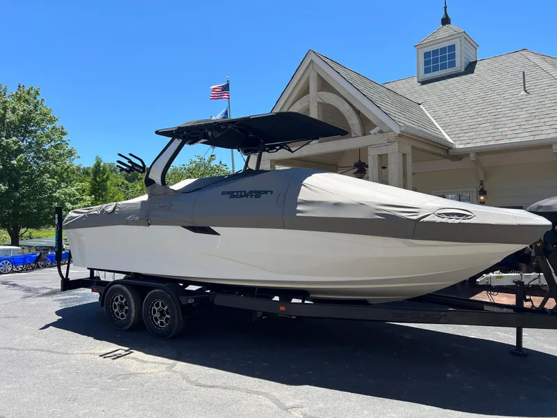 Slide: The Image of 2024 Centurion Fi23 boat on trailer, covered, parked near a building with American flag. - 24