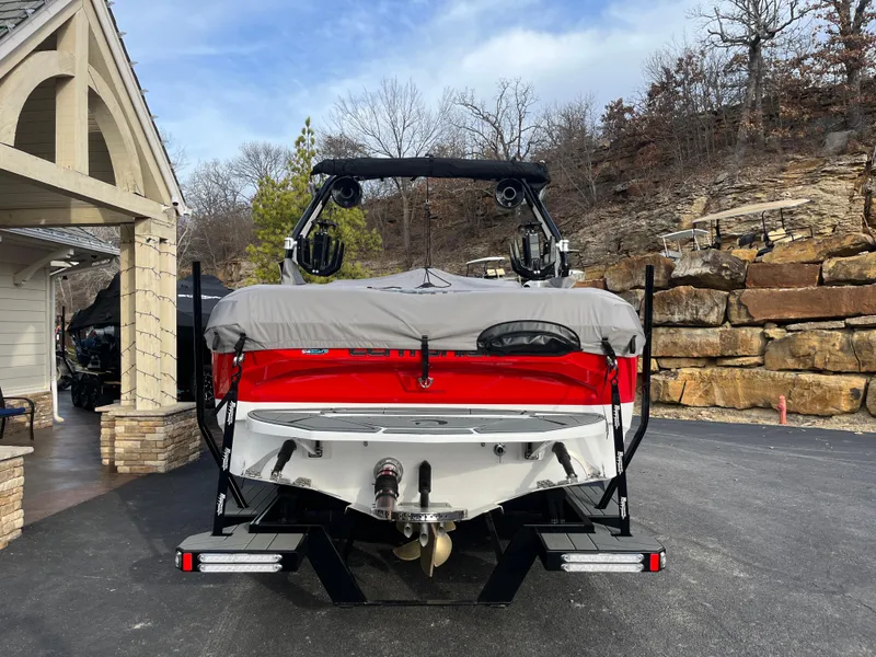 Slide: The Image of 2025 Centurion NV233 boat with cover, parked on driveway near stone wall. - 14