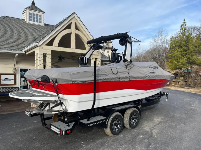 Slide: The Image of 2025 Centurion NV233 boat with cover on trailer, parked near a house. - 15