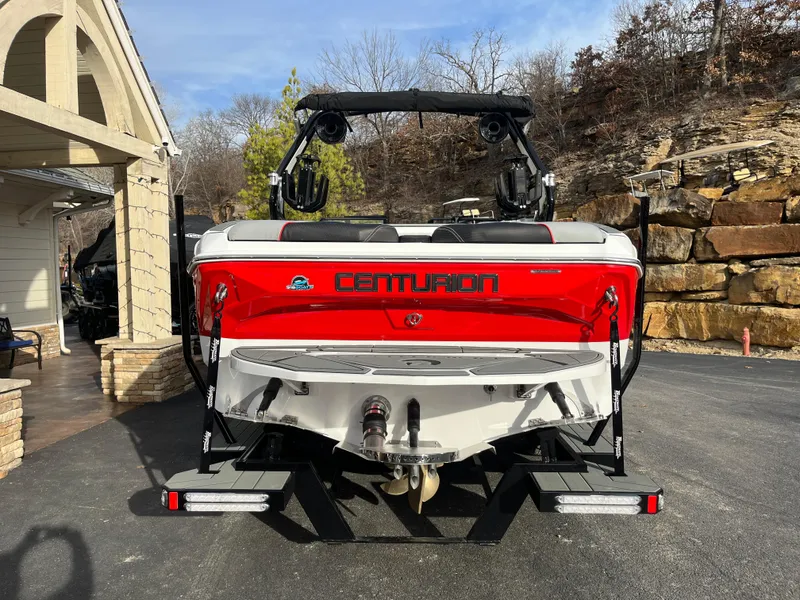 Slide: The Image of 2025 Centurion NV233 boat, red and white, parked on driveway near stone wall. - 5