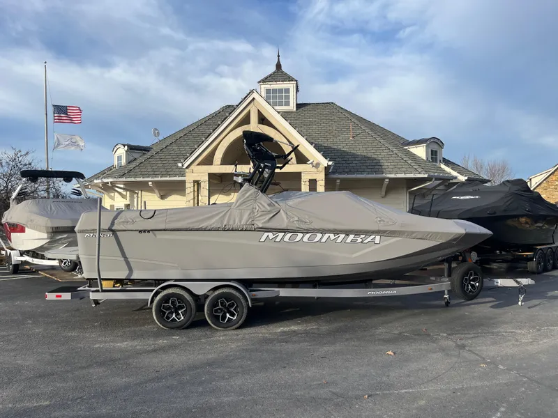 Slide: The Image of 2025 Moomba Makai boat on trailer, covered, parked outside a building with American flag. - 13