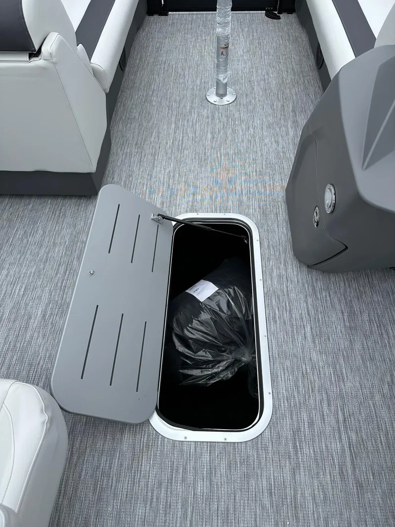 Slide: The Image of 2025 Bennington 22 SSR Tritoon storage compartment with open hatch on gray flooring. - 28