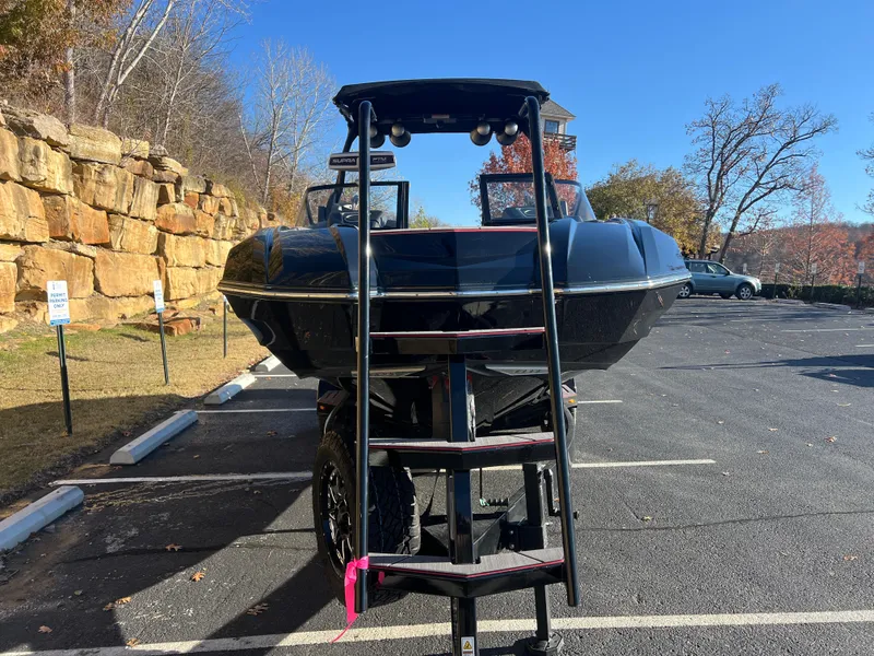 Slide: The Image of 2022 Supra SE boat on trailer in parking lot, ladder attached, sunny day. - 2