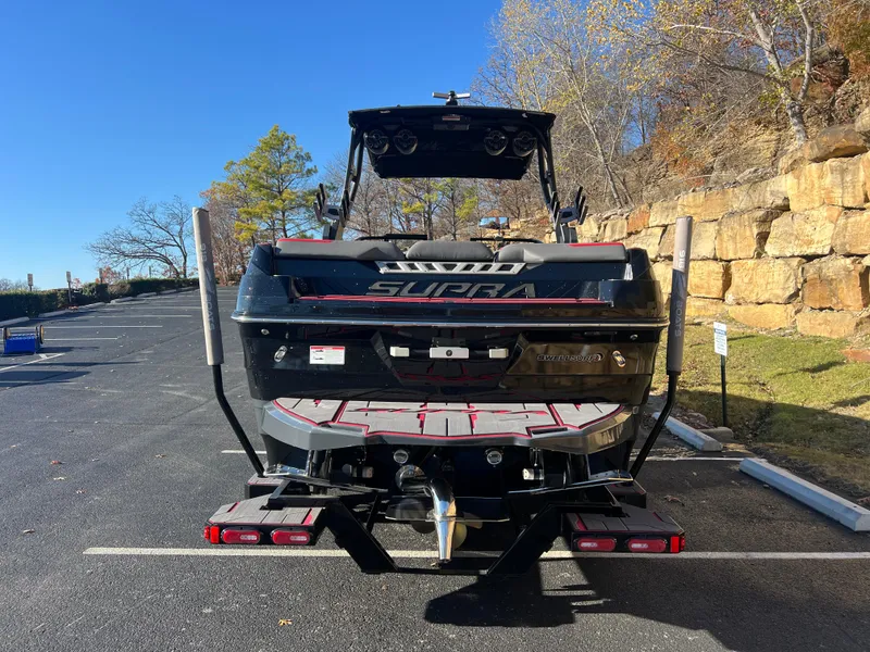 Slide: The Image of 2022 Supra SE boat parked outdoors, rear view with trailer and natural background. - 5