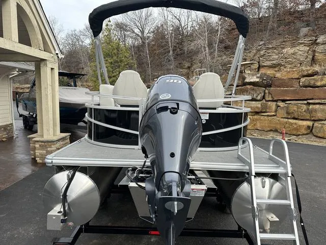Slide: The Image of 2024 Starcraft LX 20 F pontoon boat with outboard motor, parked on a driveway. - 23