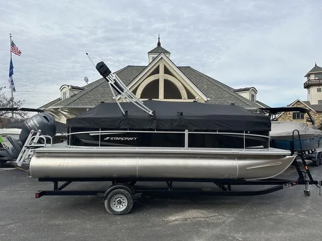 Slide: The Image of 2024 Starcraft LX 20 F pontoon boat on trailer, parked in front of a building. - 3