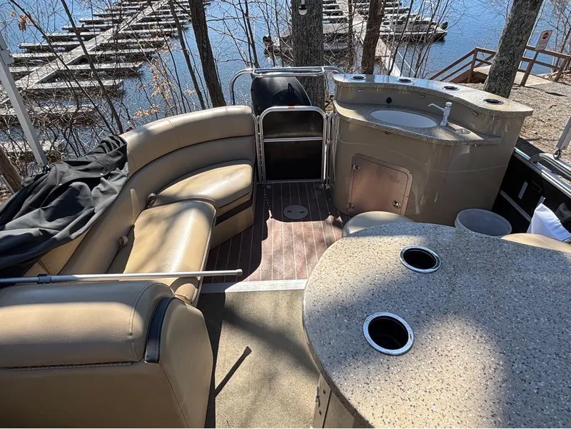Slide: The Image of 2014 South Bay 523E pontoon boat interior with seating and kitchenette, docked by a lake. - 6