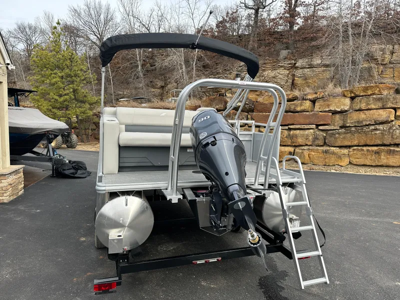 Slide: The Image of 2024 Starcraft LX 20 CB pontoon boat with outboard motor and ladder, parked on pavement. - 3