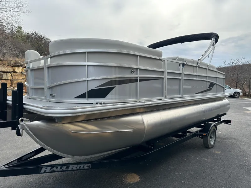 Slide: The Image of 2024 Starcraft LX 20 CB pontoon boat on trailer, silver exterior, parked outdoors. - 4