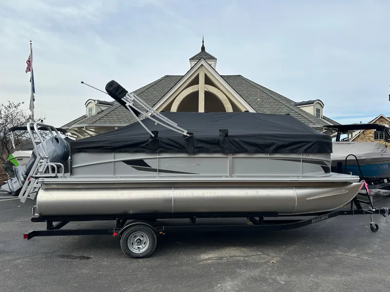 Slide: The Image of 2024 Starcraft LX 20 CB pontoon boat on trailer, covered, parked in front of a building. - 6