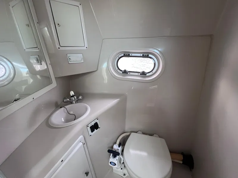 Slide: The Image of Compact bathroom in 2002 Four Winns 268 Vista boat, featuring sink, toilet, and porthole window. - 28