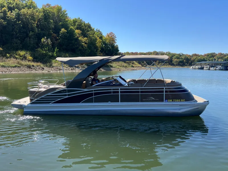 Slide: The Image of 2016 Bennington 2552 QCW I/O pontoon boat on a calm lake with lush green trees. - 0