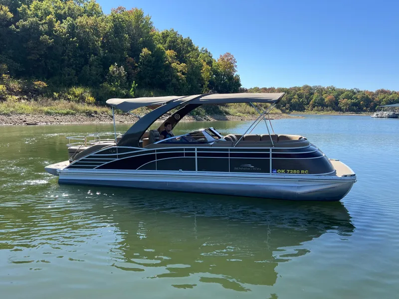 Slide: The Image of 2016 Bennington 2552 QCW I/O pontoon boat on a serene lake with lush trees. - 1