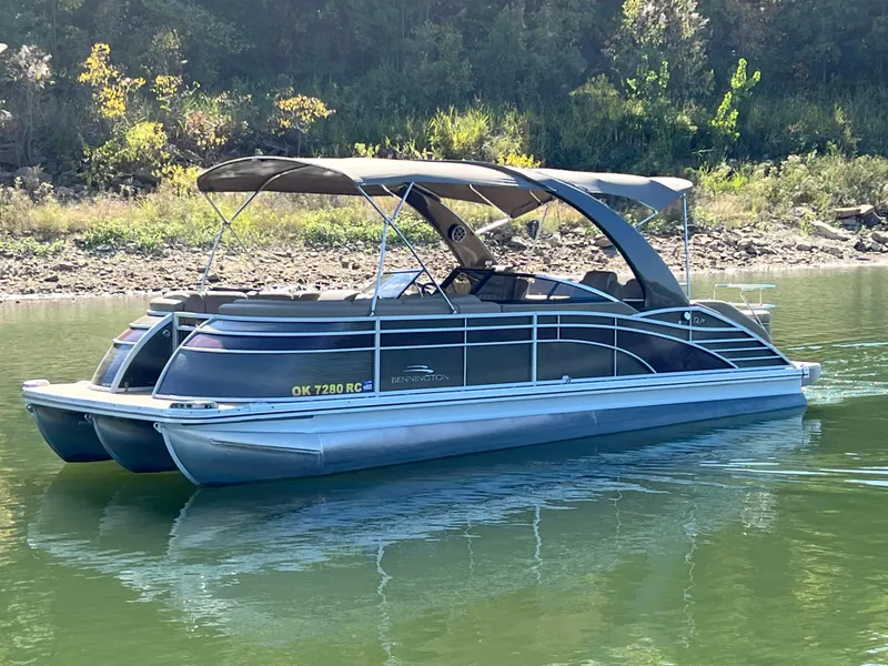 Slide: The Image of 2016 Bennington 2552 QCW I/O pontoon boat on calm water, surrounded by greenery. - 4