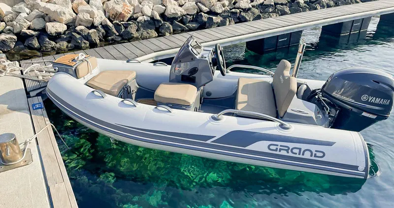 Slide: The Image of 2025 Grand Inflatables G340 boat docked, featuring Yamaha engine, clear water, and rocky shoreline. - 1