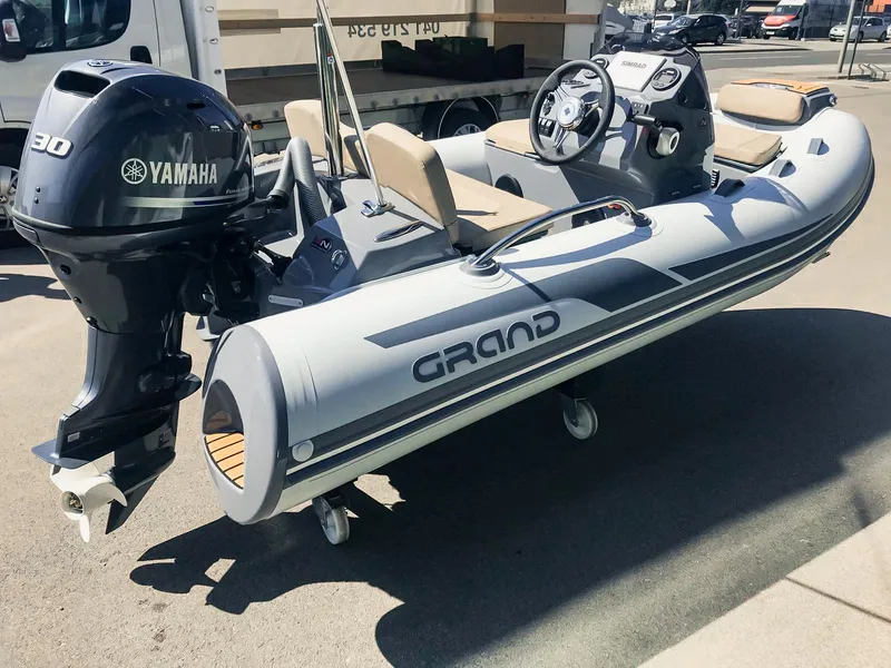 Slide: The Image of 2025 Grand Inflatables G340 boat with Yamaha engine, parked on pavement. - 2