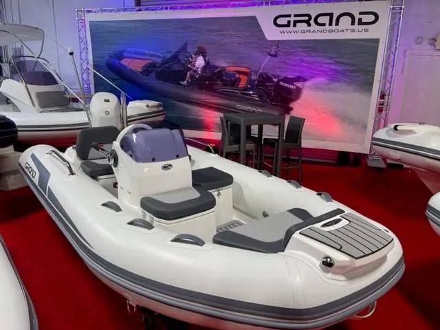 The Image of 2025 Grand Inflatables G380 boat displayed indoors on red carpet with promotional backdrop. - 0